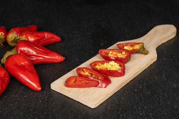 Group of six whole five slices of pickled red pepper on wooden cutting board on grey stone
