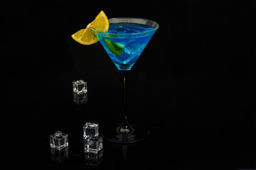 Blue cocktail in martini glasses with ice on a black background. Blue cocktail with martini and lemon on a black glass background. Cocktail blue lagoon.