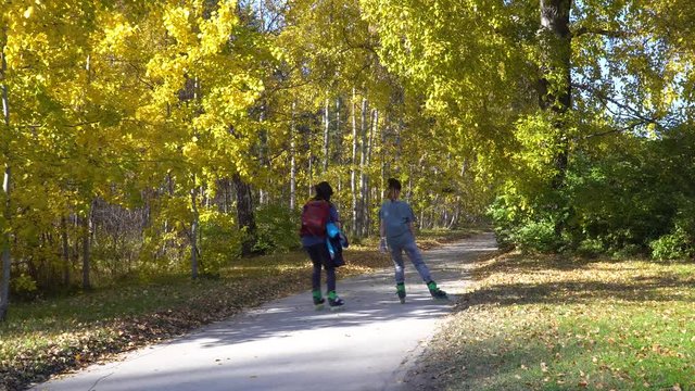 A couple of young people have fun skating on roller skates on an asphalted sidewalk in the autumn sunny day. 4k footage.