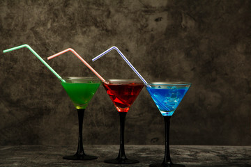 Set of blue red green cocktails in martini glasses with ice and fresh fruit kiwi pomegranate lin on a gray background. Set of cocktails with martini and fresh juice on a gray stone background.