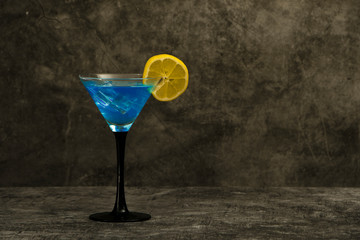 Blue cocktail in martini glasses with ice on a gray concrete background. Blue cocktail with martini on a gray stone background with lemon.