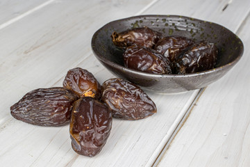 Group of eight whole dried brown date fruit in glazed bowl on white wood