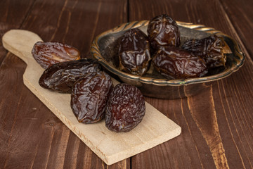 Group of eight whole dried brown date fruit on wooden cutting board in copper bowl on brown wood