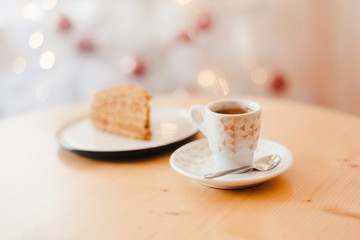 Italian coffee Cup and honey cake on the table near the Christmas tree with white bokeh