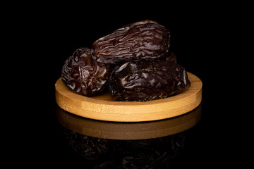 Group of three whole dried brown date fruit on round bamboo coaster isolated on black glass
