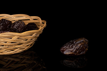 Lot of whole dried brown date fruit in round rattan bowl isolated on black glass