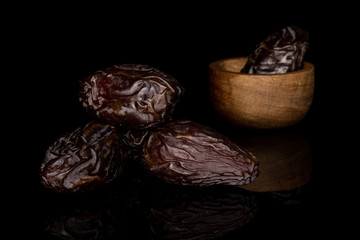 Group of four whole dried brown date fruit in bamboo bowl isolated on black glass