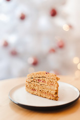 Honey cake on the table near the white Christmas tree with golden bokeh lights
