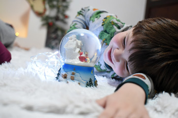 Boy looking a glass snow ball under a Christmas tree. Child with a snow ball with a New Year
