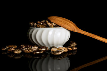 Lot of whole speckled brown bean pinto in ceramic stewpan with wooden spoon isolated on black glass