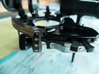 Sextant on a chart table, with a nautocal charts in background.