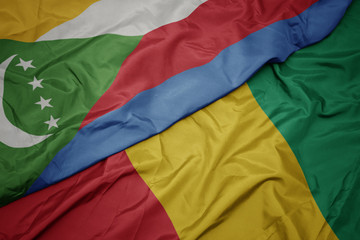 waving colorful flag of guinea and national flag of comoros.