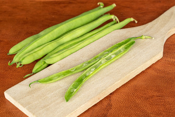 Group of two halves lot of pieces of snap green bean on wooden cutting board on cognac leather