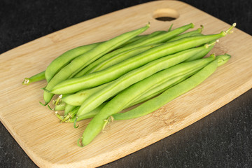Fototapeta premium Lot of whole snap green bean on bamboo cutting board on grey stone