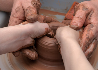 Top view of the ceramic production process on the potter wheel of an adult master and child. The concept of interesting children leisure time and creativity.