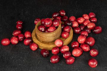 Lot of whole fresh red cranberry on round bamboo coaster in bamboo bowl on grey stone