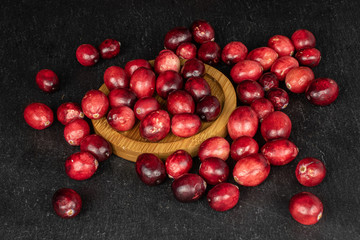 Lot of whole fresh red cranberry on round bamboo coaster on grey stone