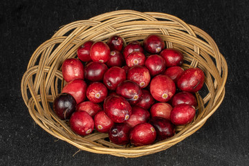 Lot of whole fresh red cranberry in round rattan bowl on grey stone