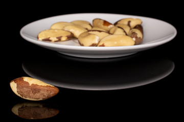 Lot of whole brazil brown nut front focus on white ceramic plate isolated on black glass
