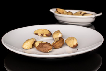 Fototapeta na wymiar Lot of whole brazil brown nut on white ceramic plate isolated on black glass