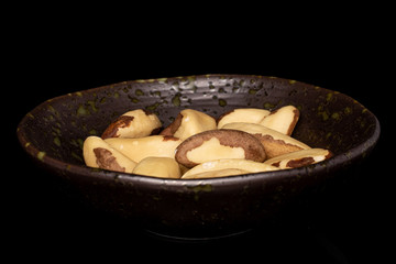 Lot of whole brazil brown nut in glazed bowl isolated on black glass