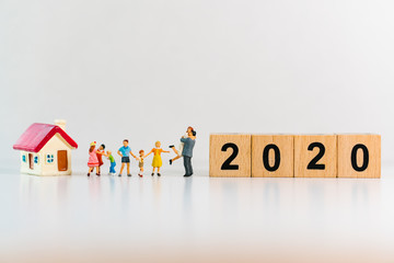 Miniature people, happy family standing with the house and wooden block 2020 using as family and...