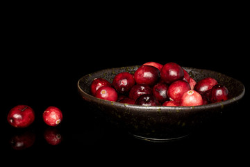 Lot of whole fresh red cranberry in glazed bowl isolated on black glass