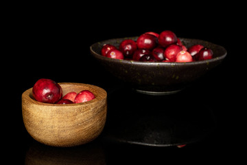 Lot of whole fresh red cranberry in glazed bowl in bamboo bowl isolated on black glass