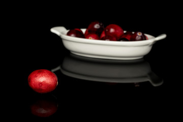 Lot of whole fresh red cranberry front focus on white ceramic plate isolated on black glass
