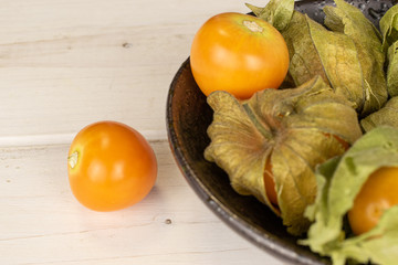 Group of six whole fresh orange physalis in glazed bowl on white wood