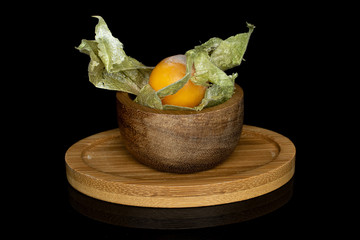 One whole fresh orange physalis in bamboo bowl on round bamboo coaster isolated on black glass