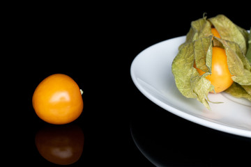 Group of three whole fresh orange physalis on white ceramic plate isolated on black glass