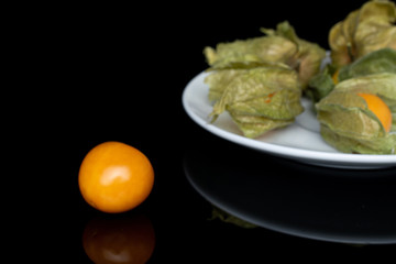 Group of five whole fresh orange physalis on white ceramic plate isolated on black glass