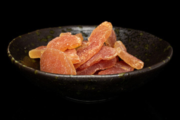 Lot of whole dried orange papaya piece in glazed bowl isolated on black glass