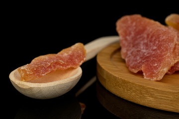 Group of three whole dried orange papaya piece with wooden scoop on round bamboo coaster isolated on black glass