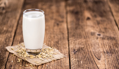 Old wooden table with fresh Oat Milk (close-up shot; selective focus)