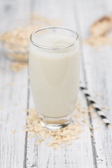 Old wooden table with fresh Oat Milk (close-up shot; selective focus)
