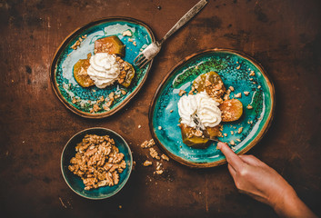 Fototapeta na wymiar Turkish traditional pumpkin dessert. Flat-lay of pumpkin in sweet syrup with cinnamon, walnuts, whipped cream and womans hand cutting piece, top view. Middle East oriental cuisine typical vegan food