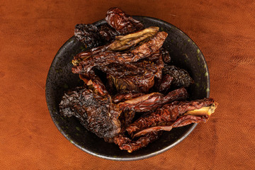 Lot of whole dried red tomato piece in glazed bowl flatlay on cognac leather