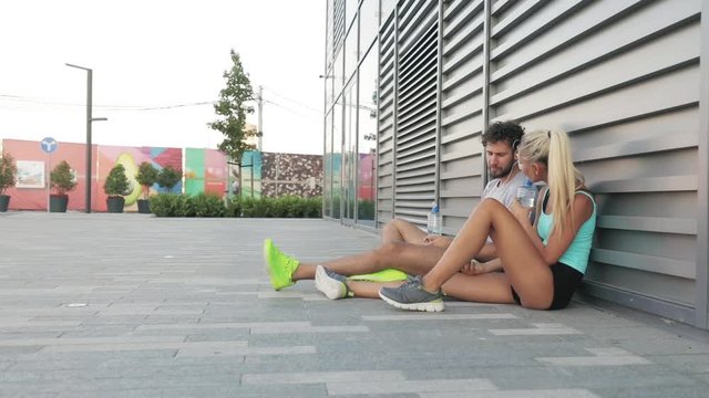 Modern young man and woman making pause after jogging / exercise in urban area.