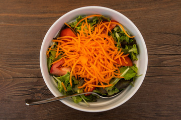 Salad of fresh vegetables in a white dish placed on an old wooden table top view