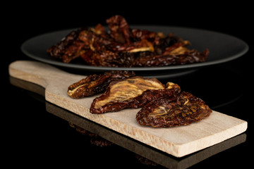 Lot of whole dried red tomato piece on gray ceramic plate on wooden cutting board isolated on black glass
