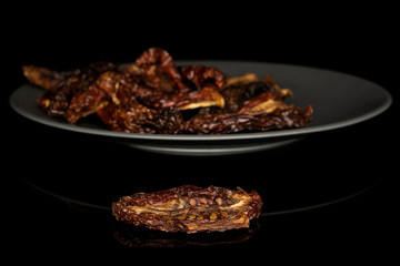 Lot of whole dried red tomato piece on gray ceramic plate isolated on black glass