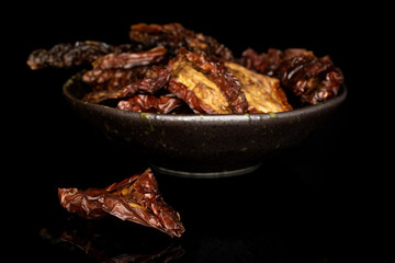 Lot of whole dried red tomato piece front focus in glazed bowl isolated on black glass