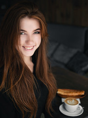 Cute redhead woman woman with adorable smile sitting in cozy city cafe enjoying free time coffee break with cappuccino and dessert
