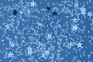 Delicate glitter star confetti on blue background. Creative and moody color of the picture.