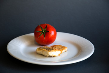  On a plate a slice of fish whole tomatoes