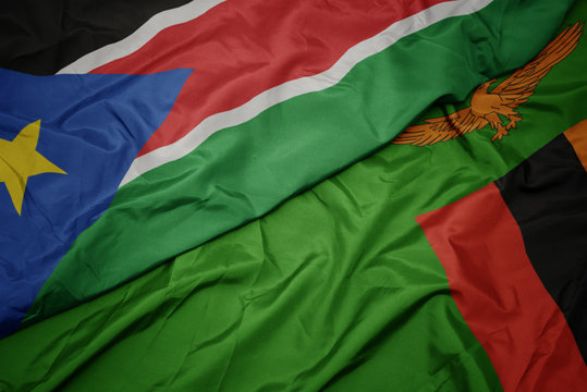waving colorful flag of zambia and national flag of south sudan.