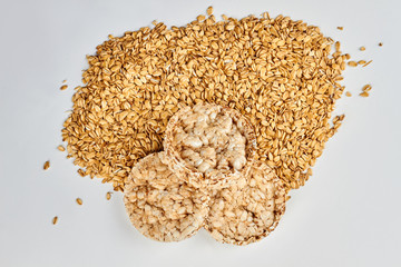 Round crispbread and oat flakes. Crunchy cereal crispbread and heap of oatmeal flakes on white background.