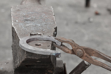 The blacksmith hold an iron horseshoe with a tongs, forging on the anvil.